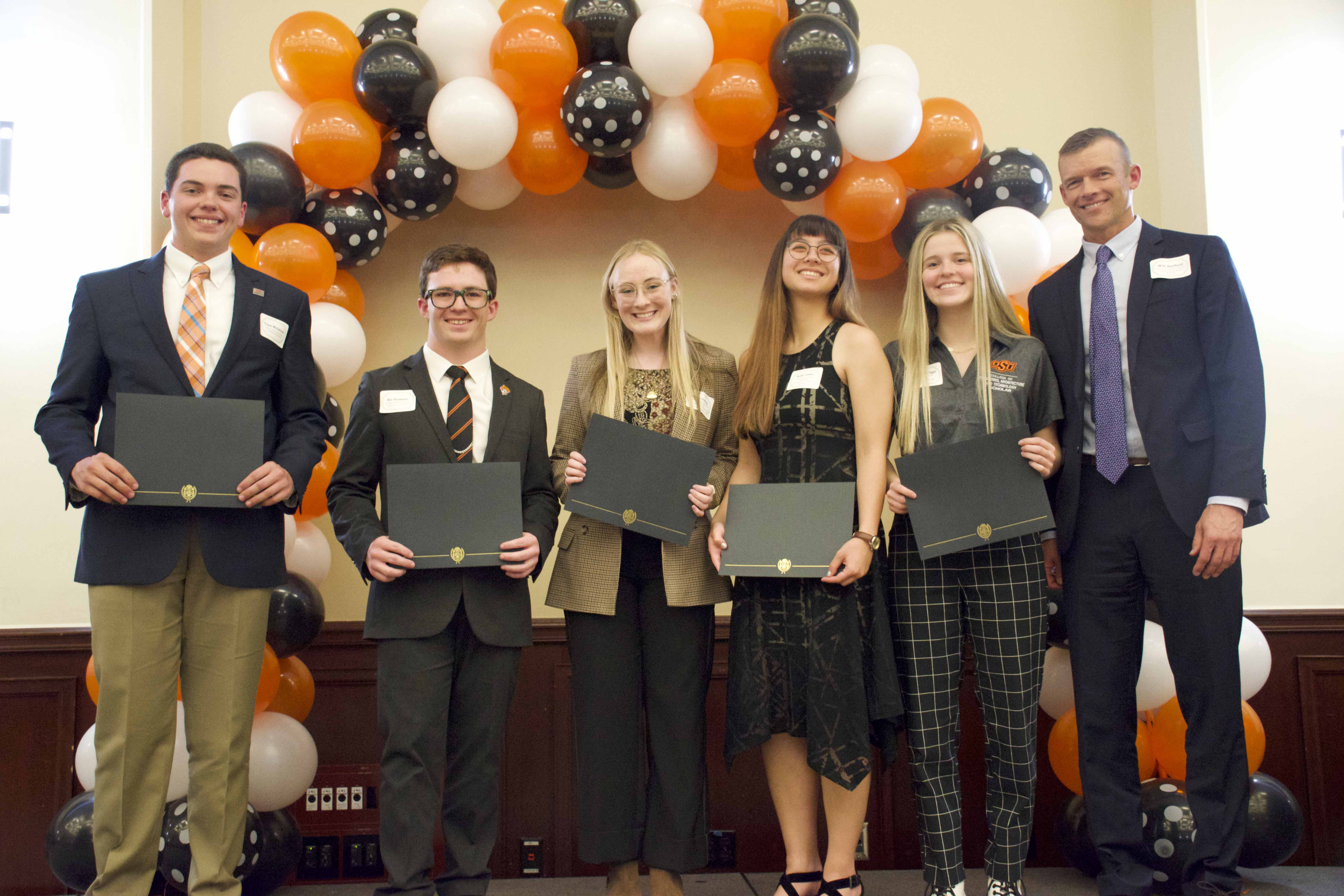 A group of students holding certificates in front of a balloon arch.
