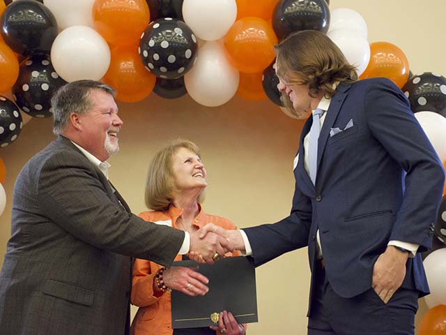 A man and woman shaking hands with a boy receiving a scholarship.