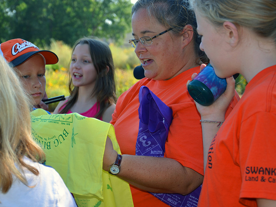 youth and instructor Dr. Shelley Mitchell explaining a bug bingo game to campers.
