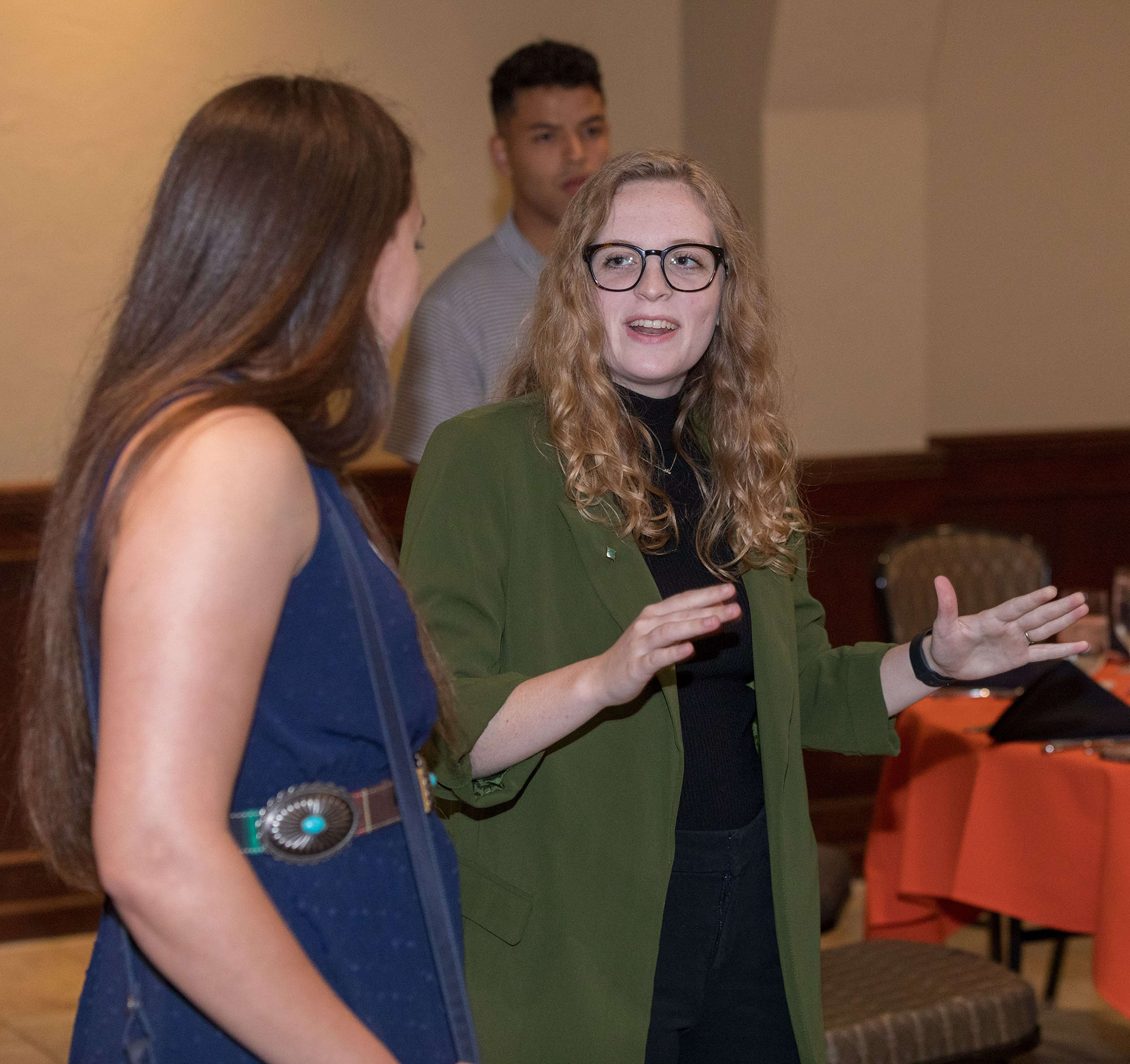 A lady with green jacket raising her hands and talking to a lady in a blue dress.