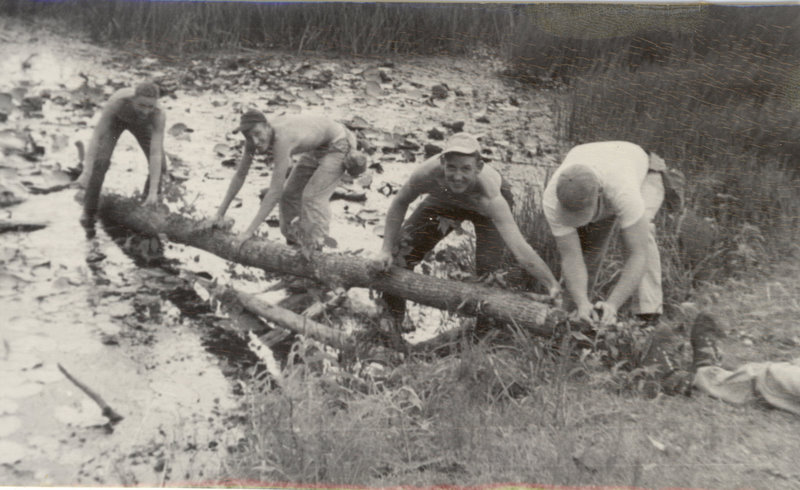 Students are bent over a log in the creek trying to move it.