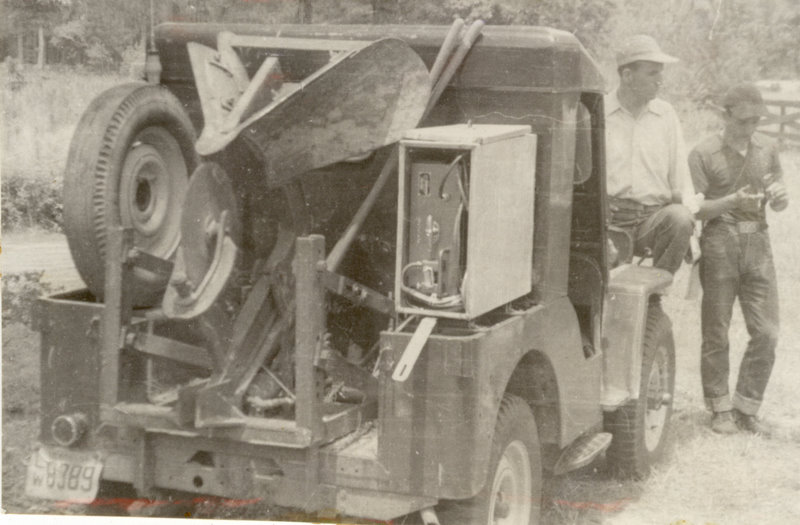 Two people are standing at the front of a farm truck.