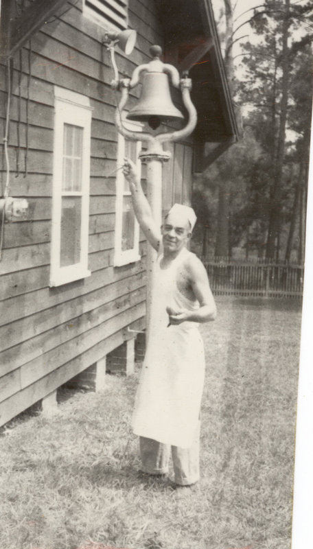 A person with an apron and chef hat stands outside ringing a bell attached to the cabin.