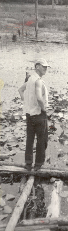 A man is standing on a wooden plank over a wet, muddy area.