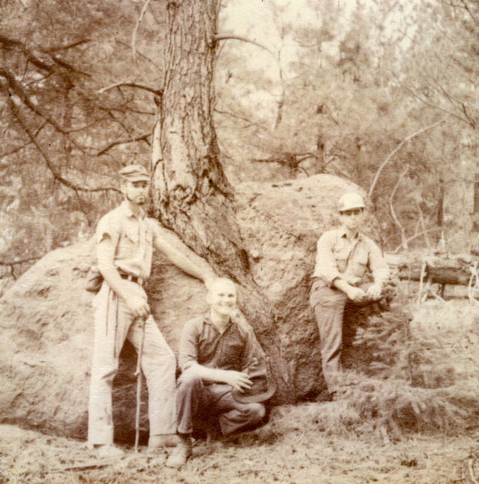 Three students posting near a rock outside.