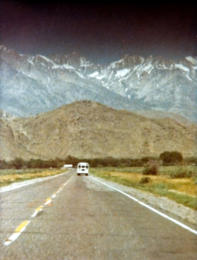 Scenic of the university van making its way down the road, against a mountain backdrop.