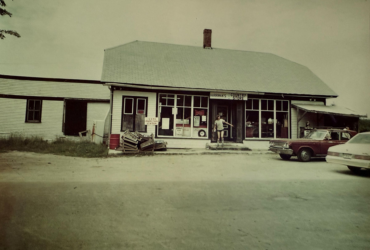 A kid coming out of a store with two cars parked out front.