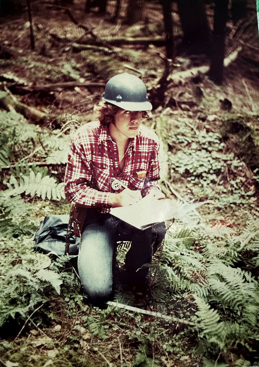 A person kneeling with a clipboard taking notes in the forest.