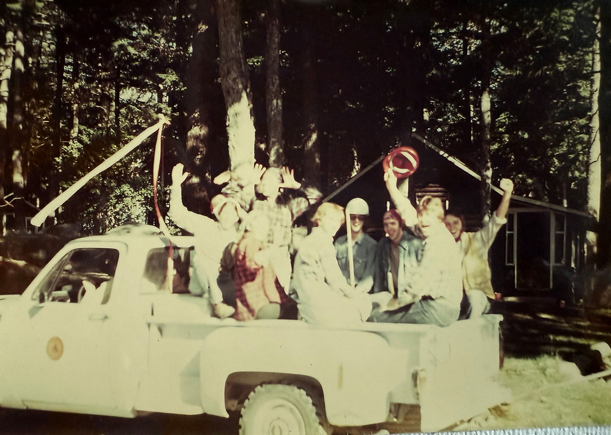 A group of people sitting and waving in the back of a pickup truck.