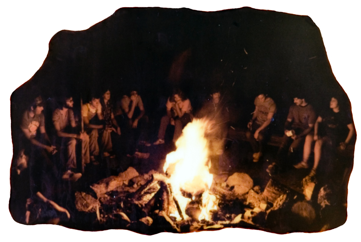 A group of people sitting around a camp fire at night.