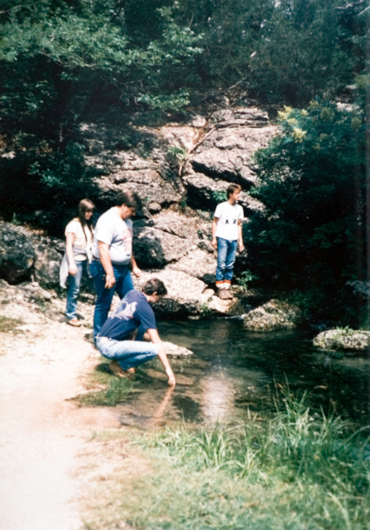 Four students taking a break next to a bed of water in the forest.