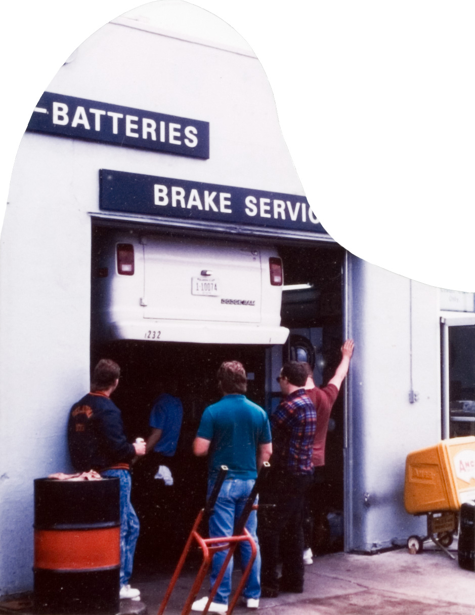Four students peering inside of a garage as gthey watch a mechanic work on a car.