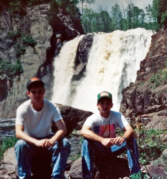 Two students pose for a photo at the bottom of a waterfall.