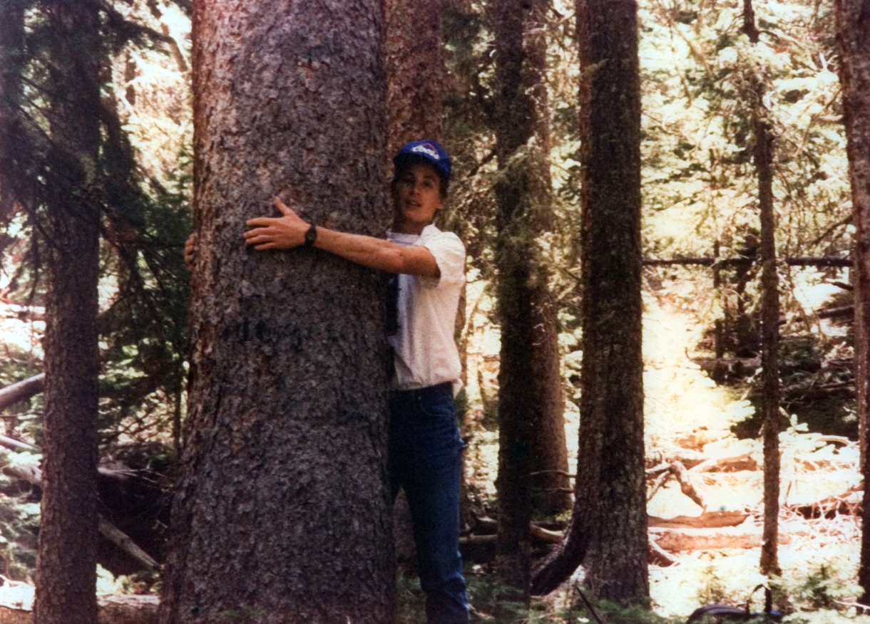 Student takes a photo hugging a tree in the woods.