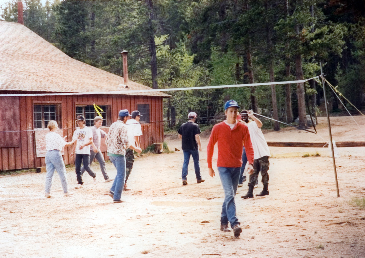 Students part into teams as they prepare for a game of volleyball next to a cabin.
