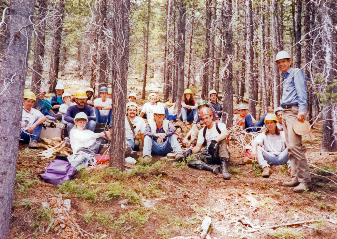 Students in hardhats take a break on a hill in the woods.