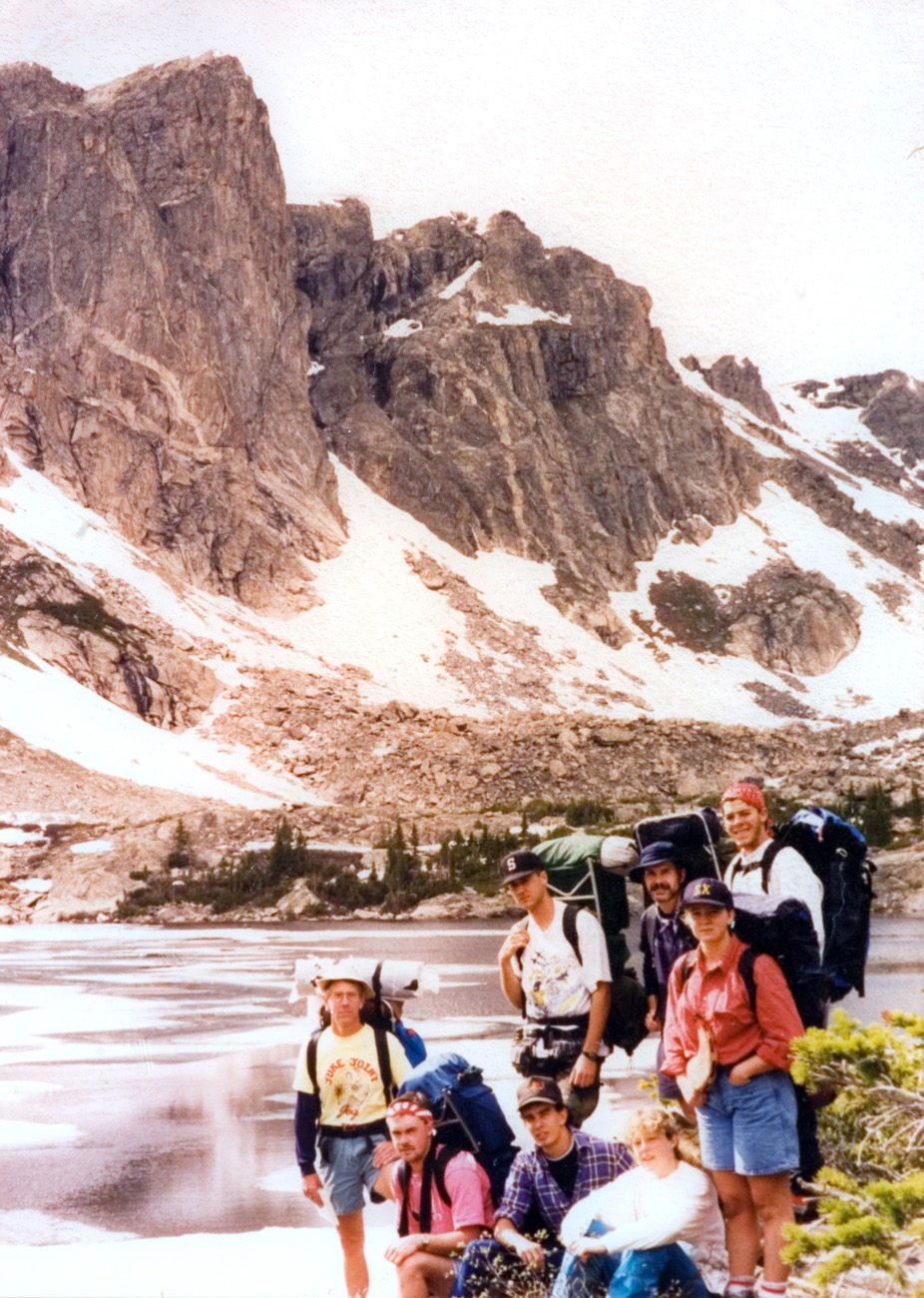Students take a break during a hike for a photo against a scenic mountain backdrop with a lake below.