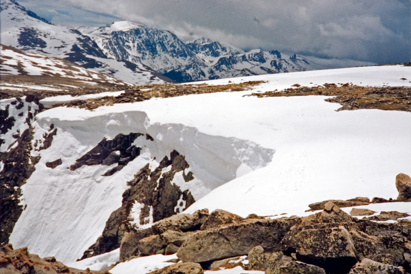 A landscape view of a snow-covered rock formation iwth snow-covered mountain tops in the background.