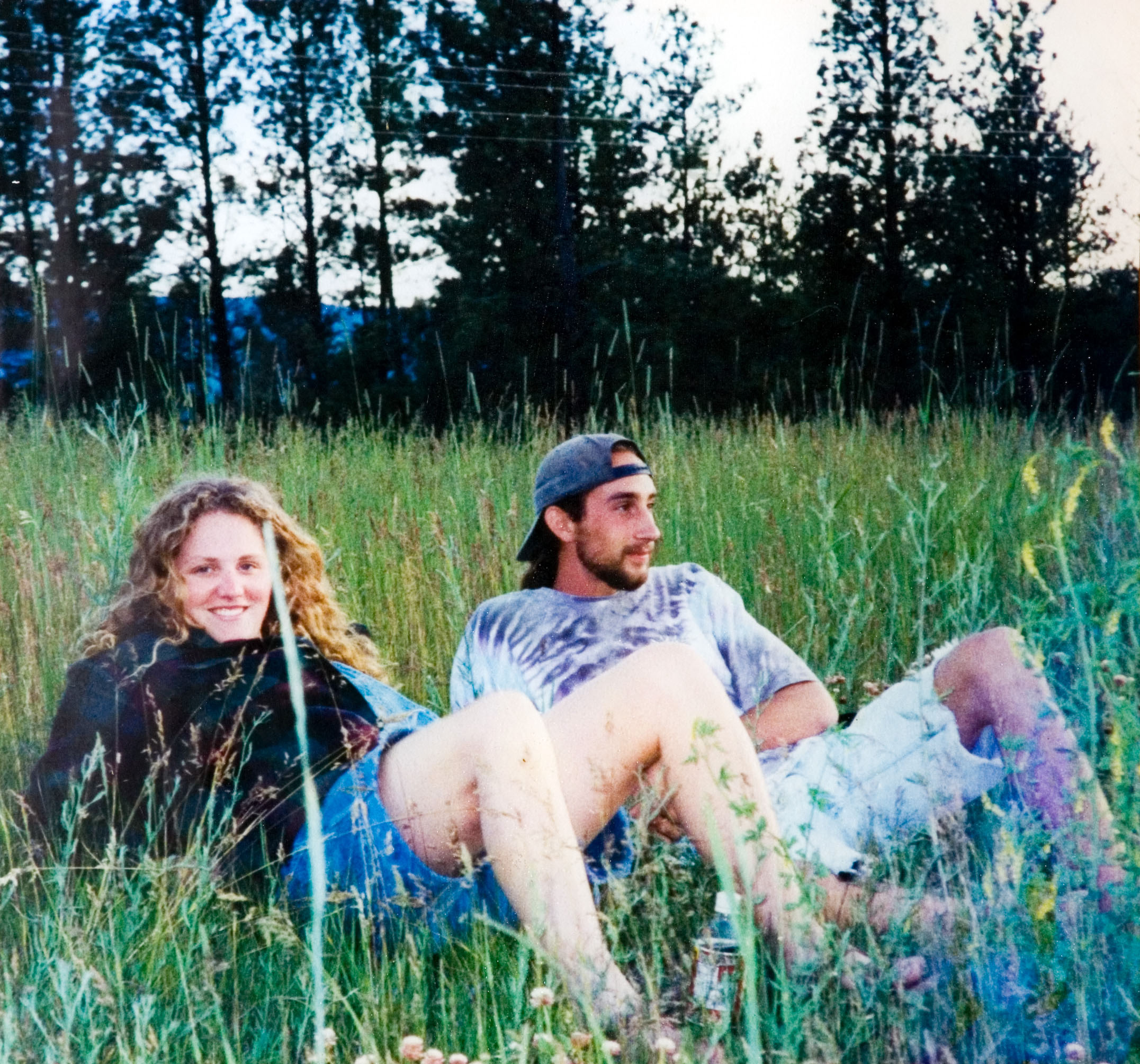 Two students laying in a bed of tall green grass as they rest.