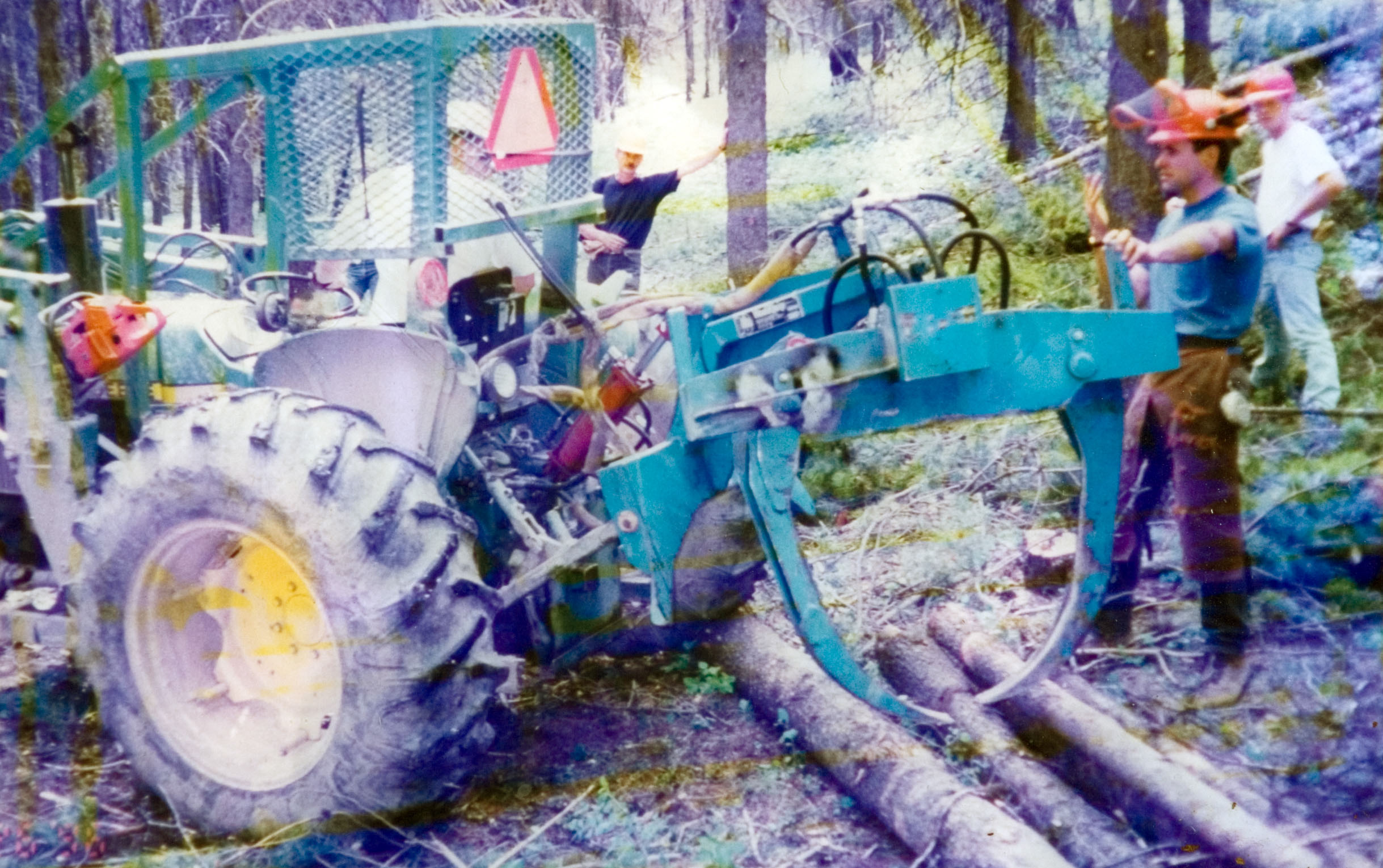 A group of students in hardhats watch an operator using a green tractor inside a forest to attend to the trees.
