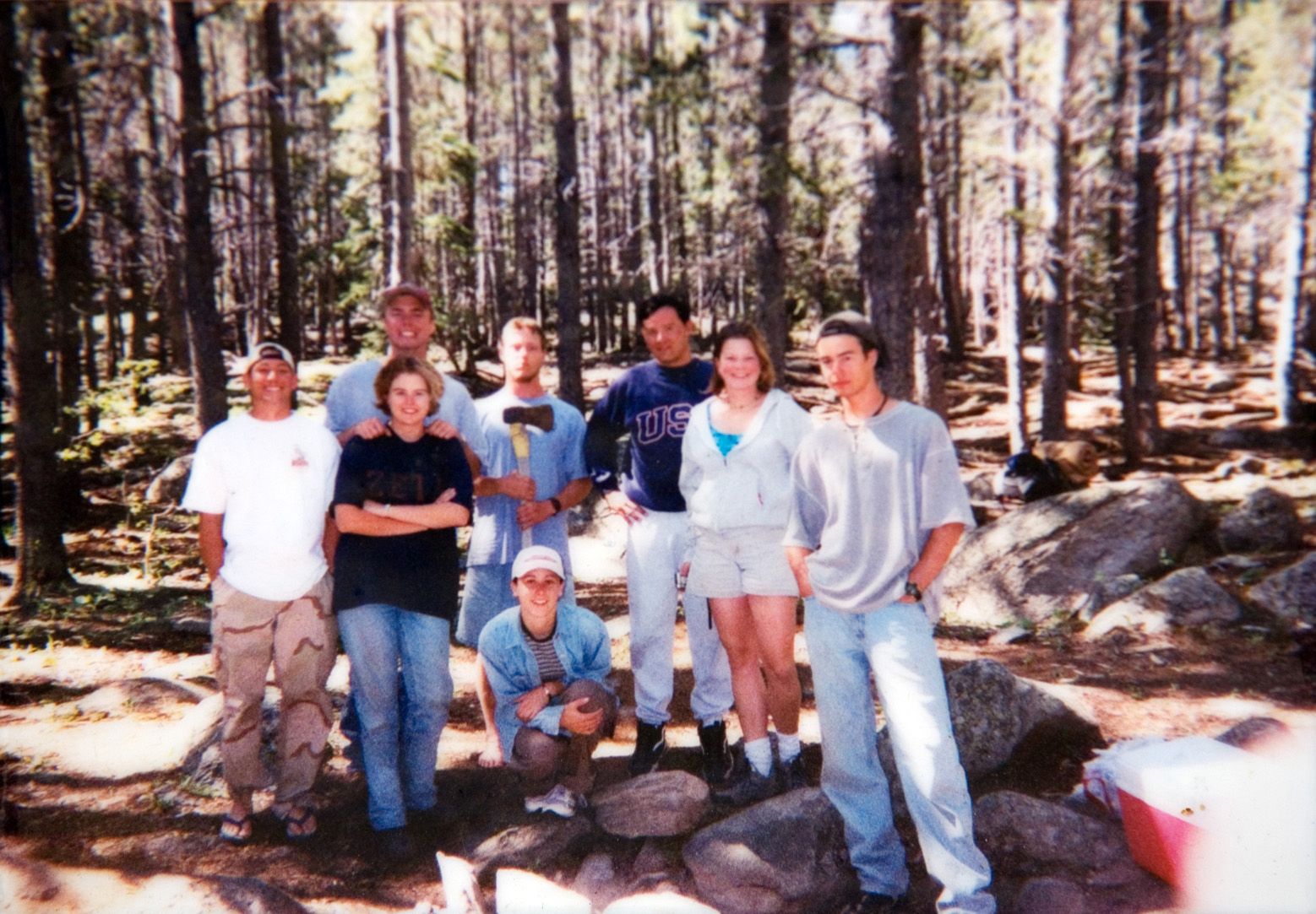 A group of eight students standning in a forest with tall trees for a group photo to be taken.