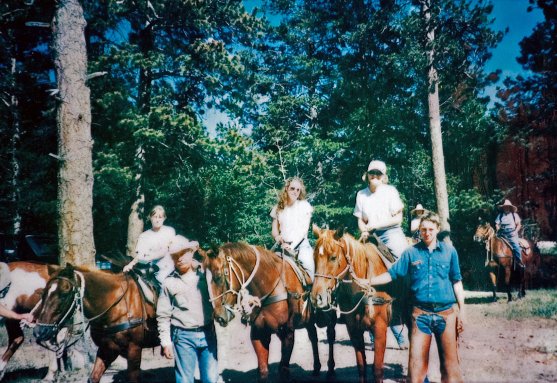 Three students on brown horses next to two instructors as they prepare to go for a horseback ride.