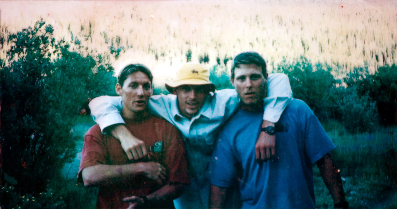 A group of three students standing outside in the green woods as they get their photo taken.