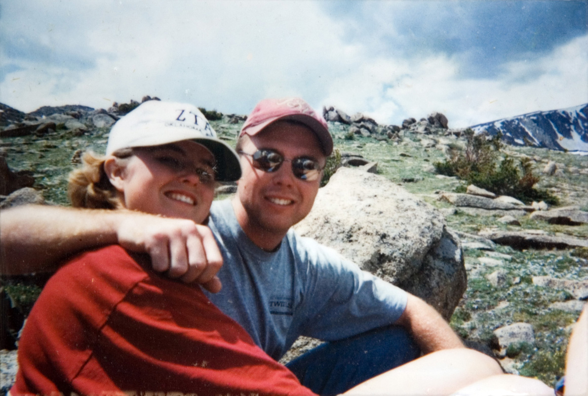 A male student in sunglasses and a female student sitting on a bed of rocky hills as they smile for their photo to be taken.