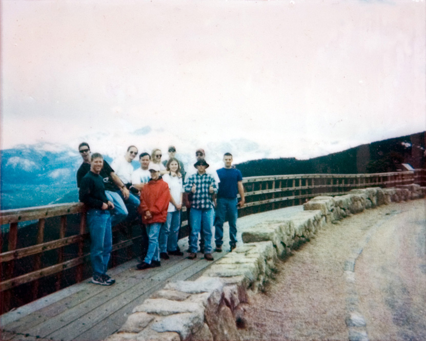 A group of 11 students standing next to a trail guard rail with a mountain range behind them as they pose for a photo in the outdoors.