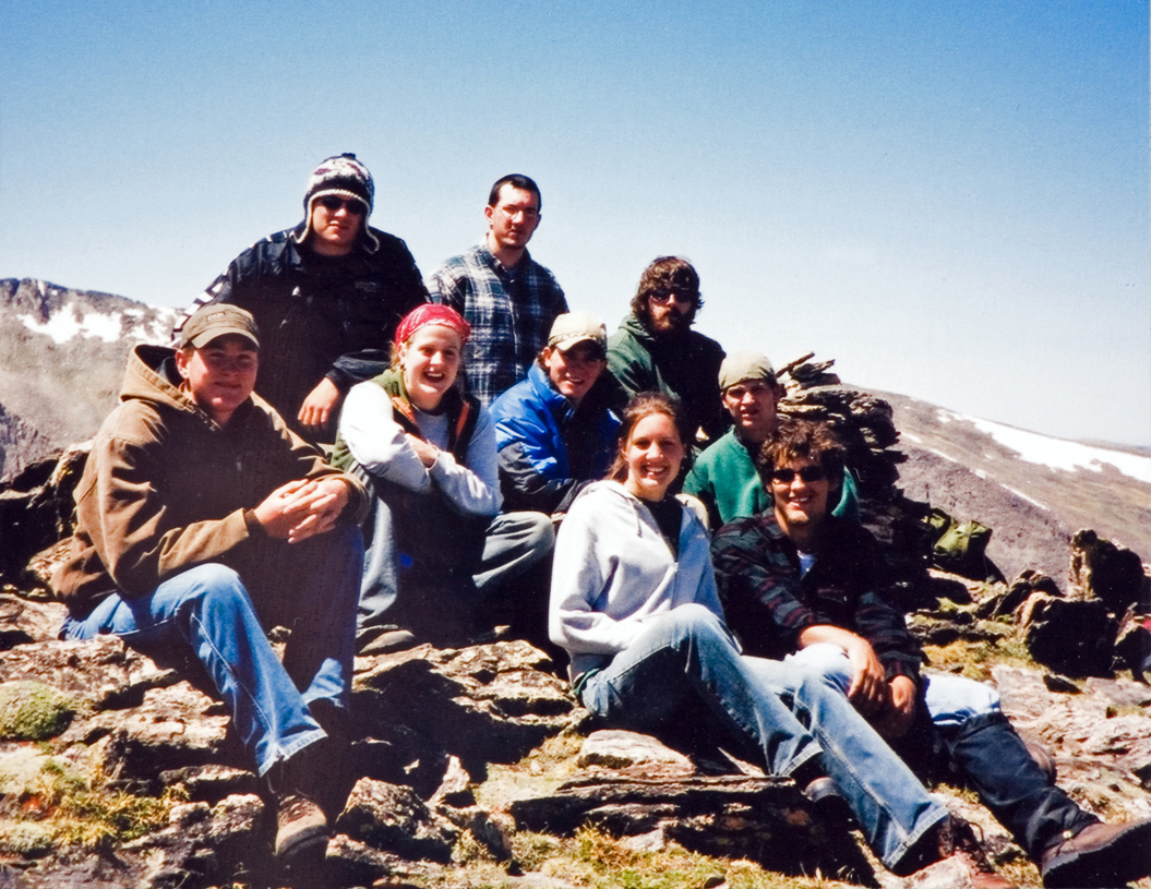 A group of students sitting on a rock during a hike as they listen to an instructor give a lesson.