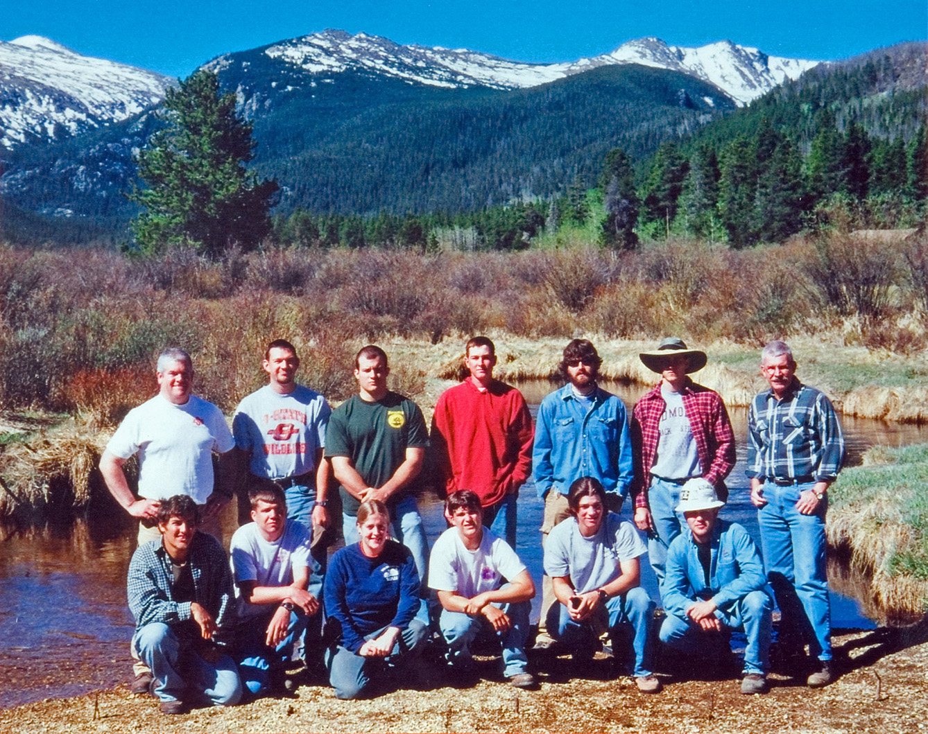 A group of students and instructors pose for a photo in a valley infront of a mountain range.