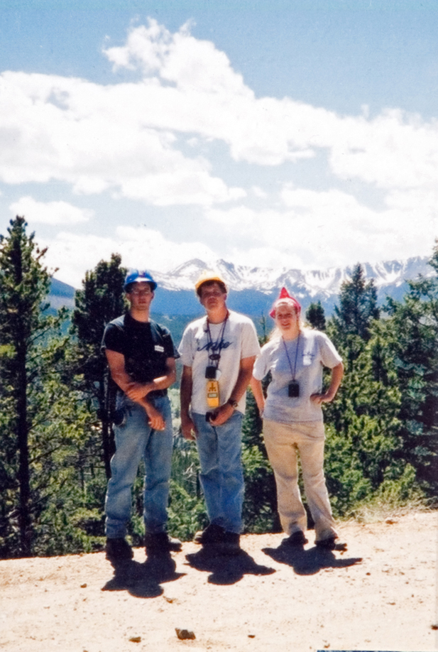 A group of three students on a hiking trail as they pose in front of a mountain.