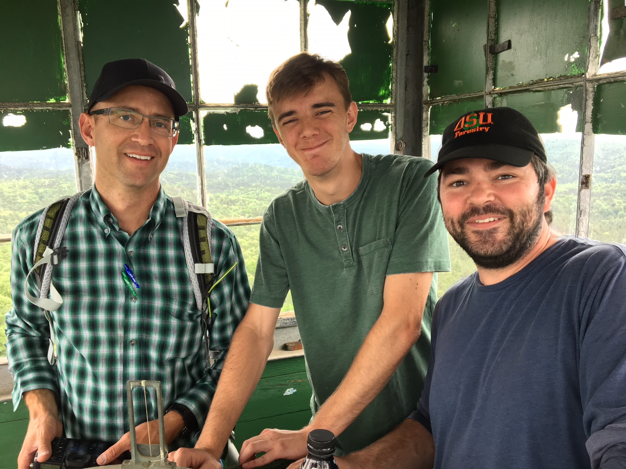 A group of three people standing at a green table smiling at the camera.