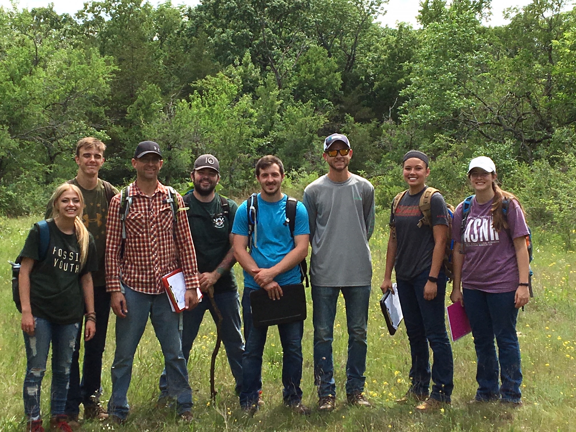 A group of eight individuals, standing in a valley, smiling at the camera.