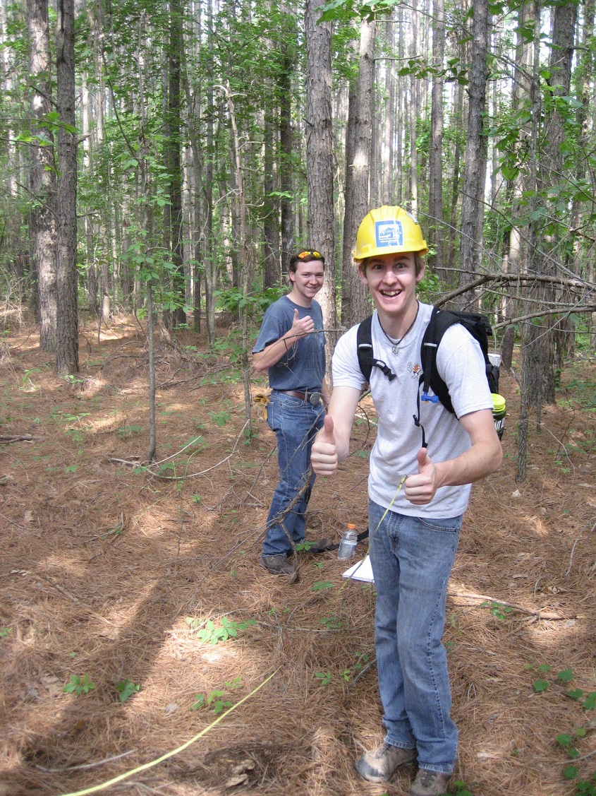 Two students standing in a wooded area giving a "thumbs up."