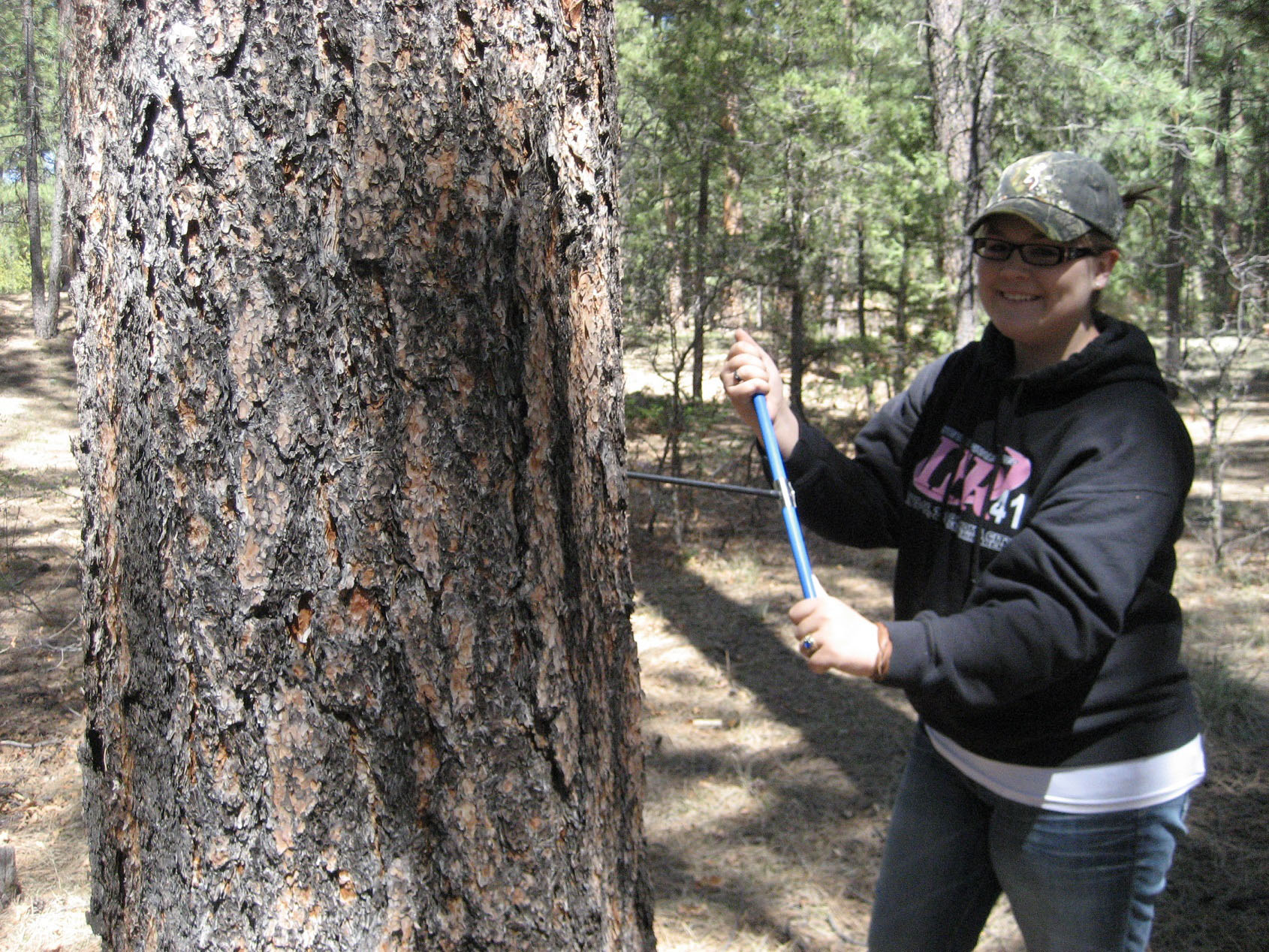 A student posing by a tree in the woods.