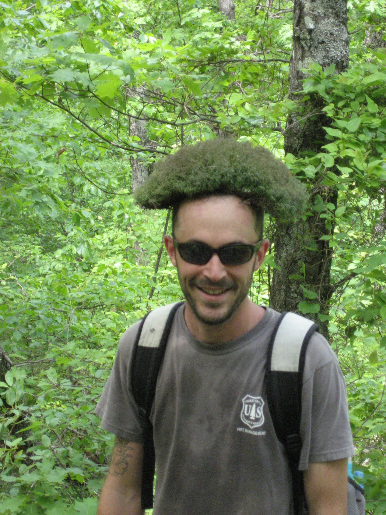 A student in the woods with a plant sitting on his head.