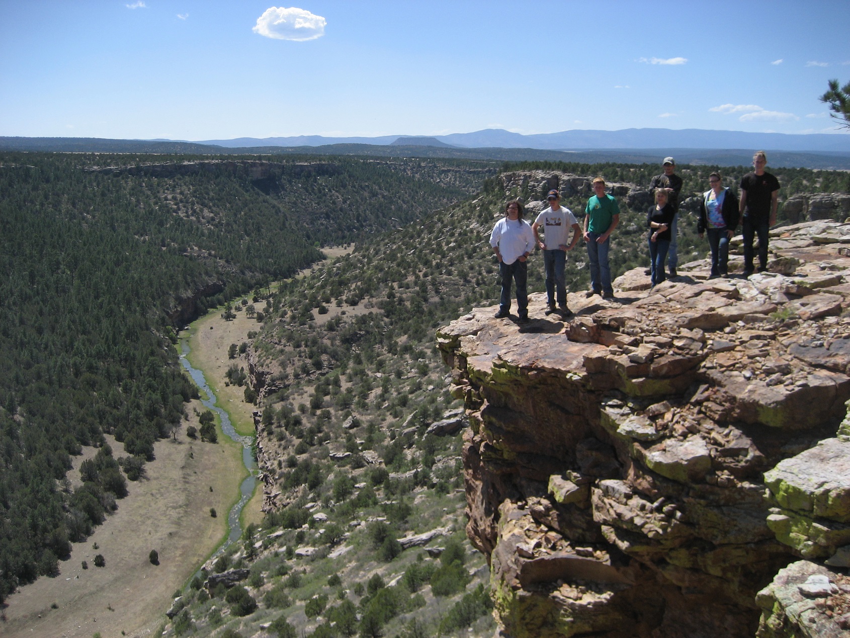 A group of students standing at the edge of a cliff overlooking a stream below.