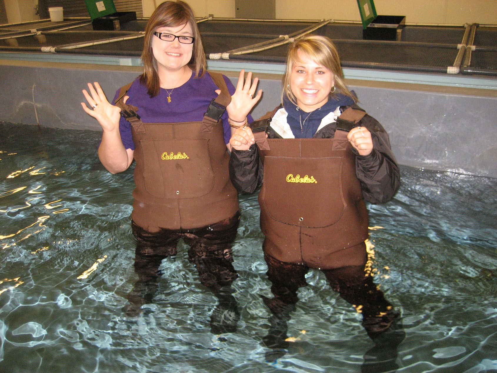Two students posing in a tank of water with waders on.