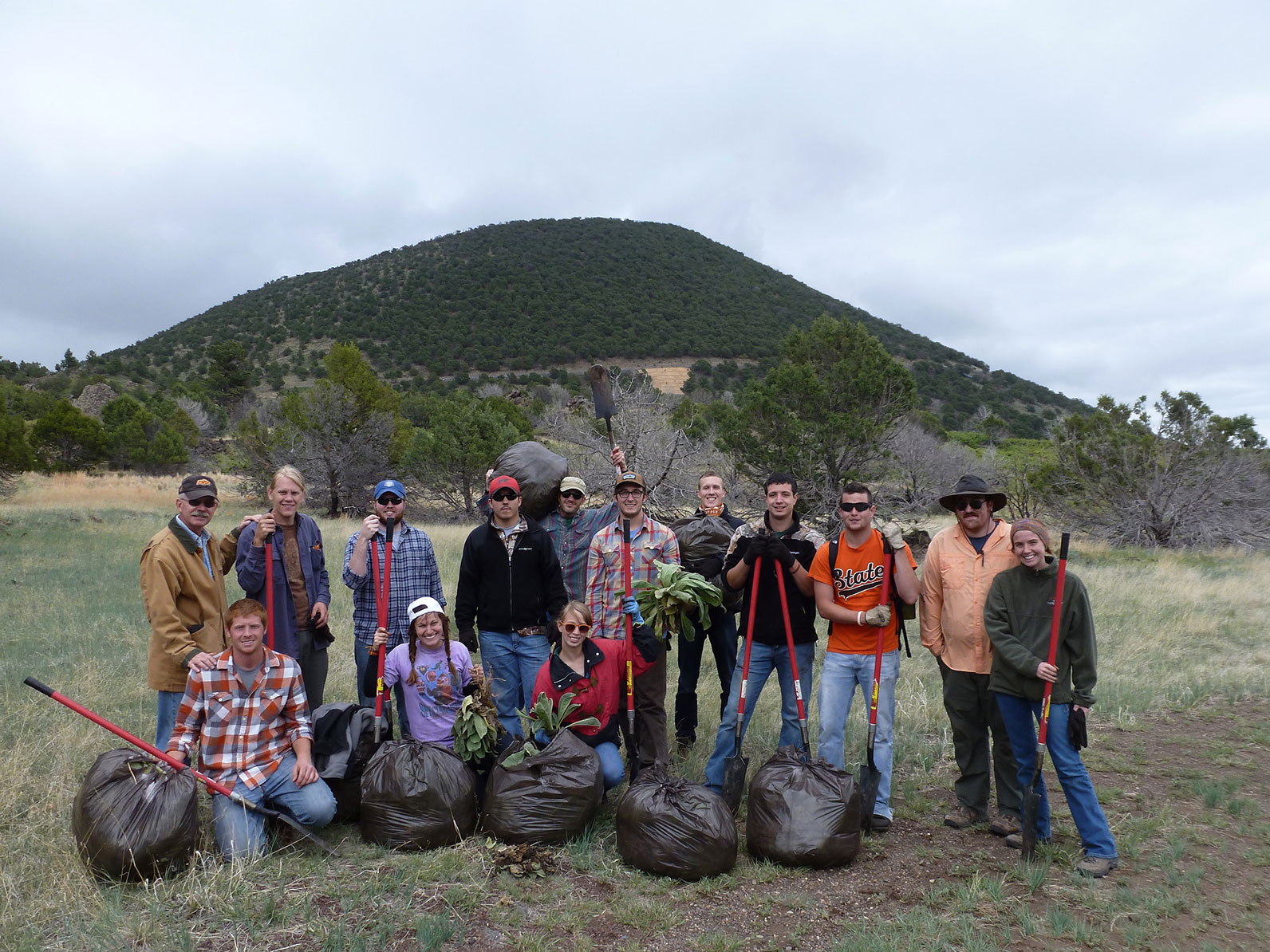 A group of participants standing and kneeling in a valley with shovels and trashbags.