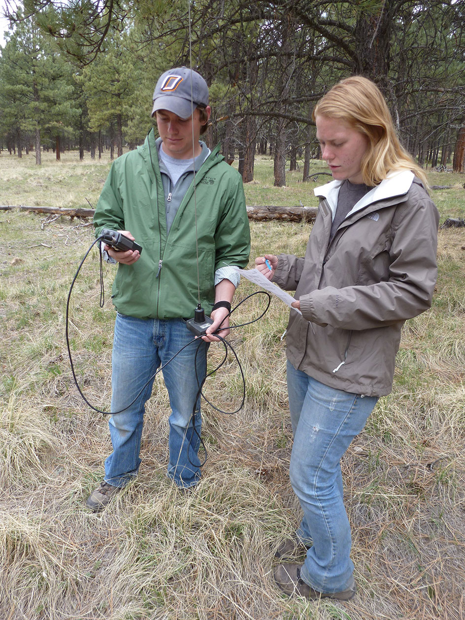 Two participants in a field using equipment to collect information.