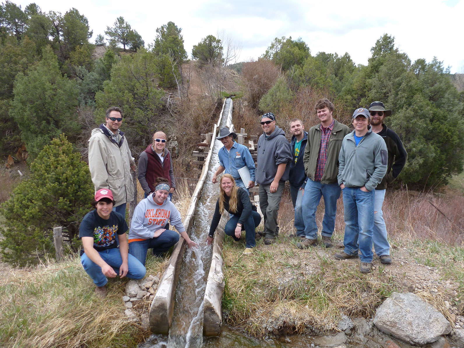 A group of participants posing by a man-made stream in a wooded area.