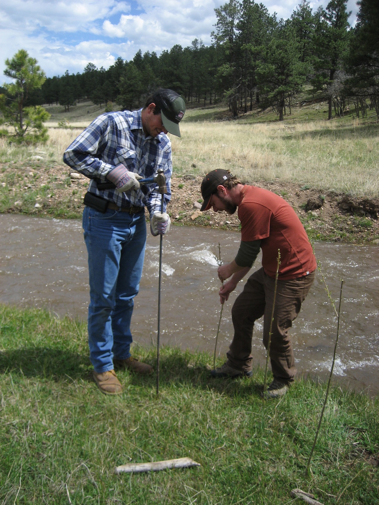 Two participants hammering stakes into the ground next to a stream in a valley.
