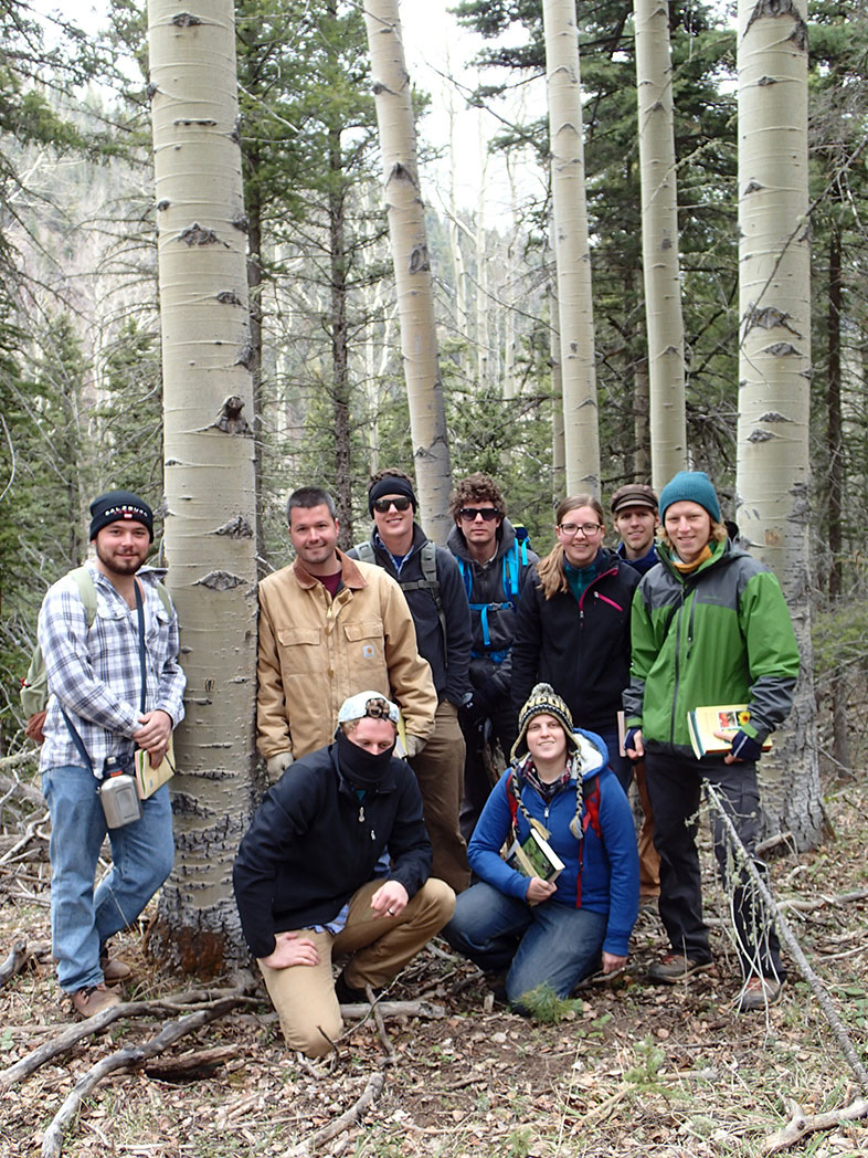 A group of nine people standing for a group photo by trees in a forest.