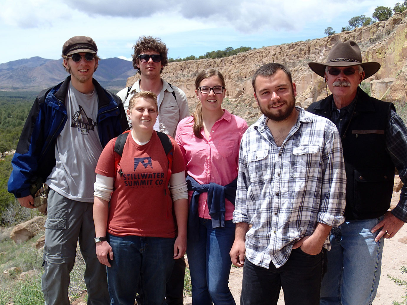 A group photo of six people standing in front of foothills.