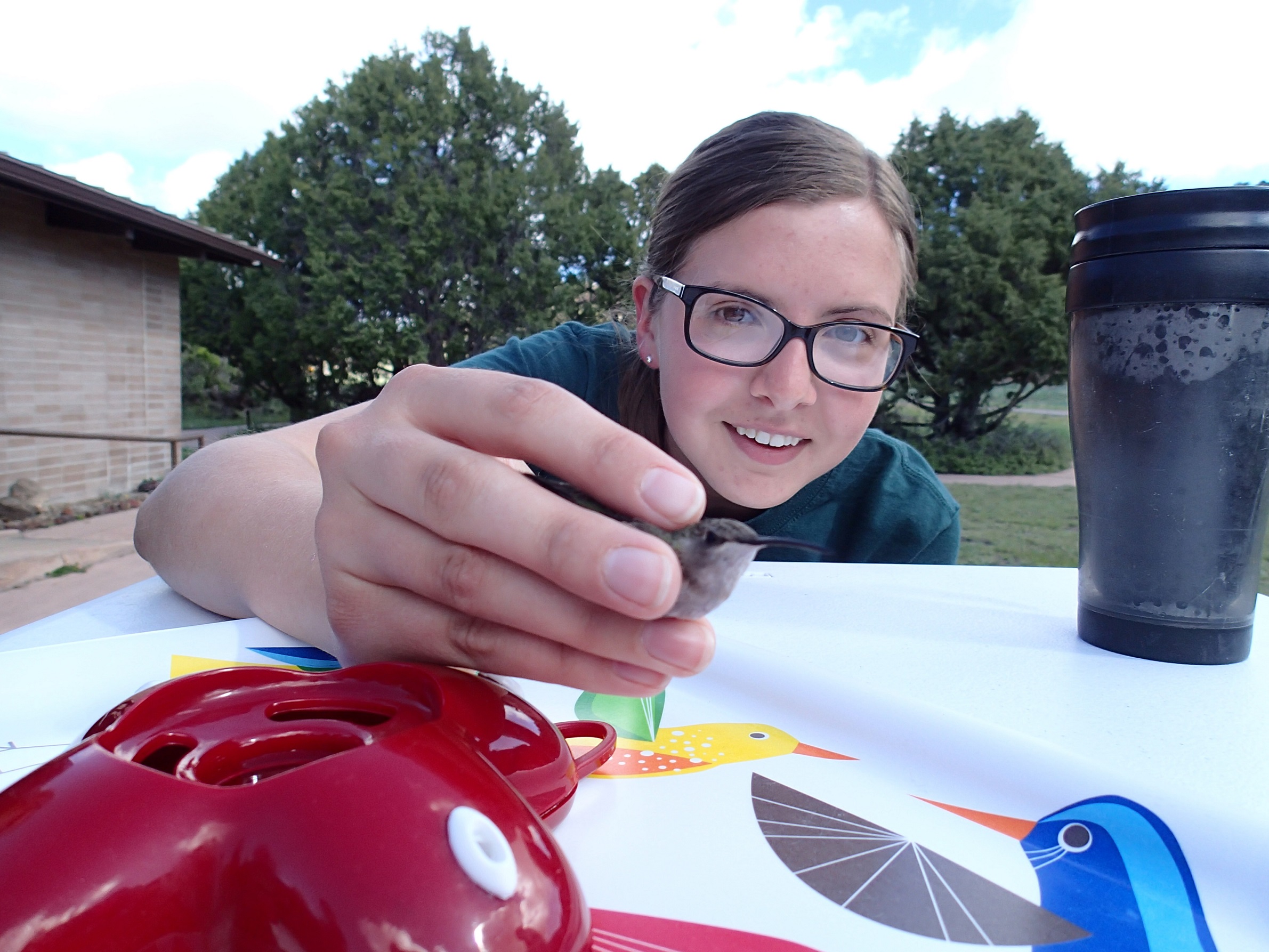 A participant with glasses posed at table with birdfeeder holding a bird in her hand.