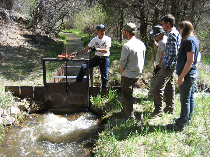 Four students receiving information from an instructor over a stream with a manual dam device.