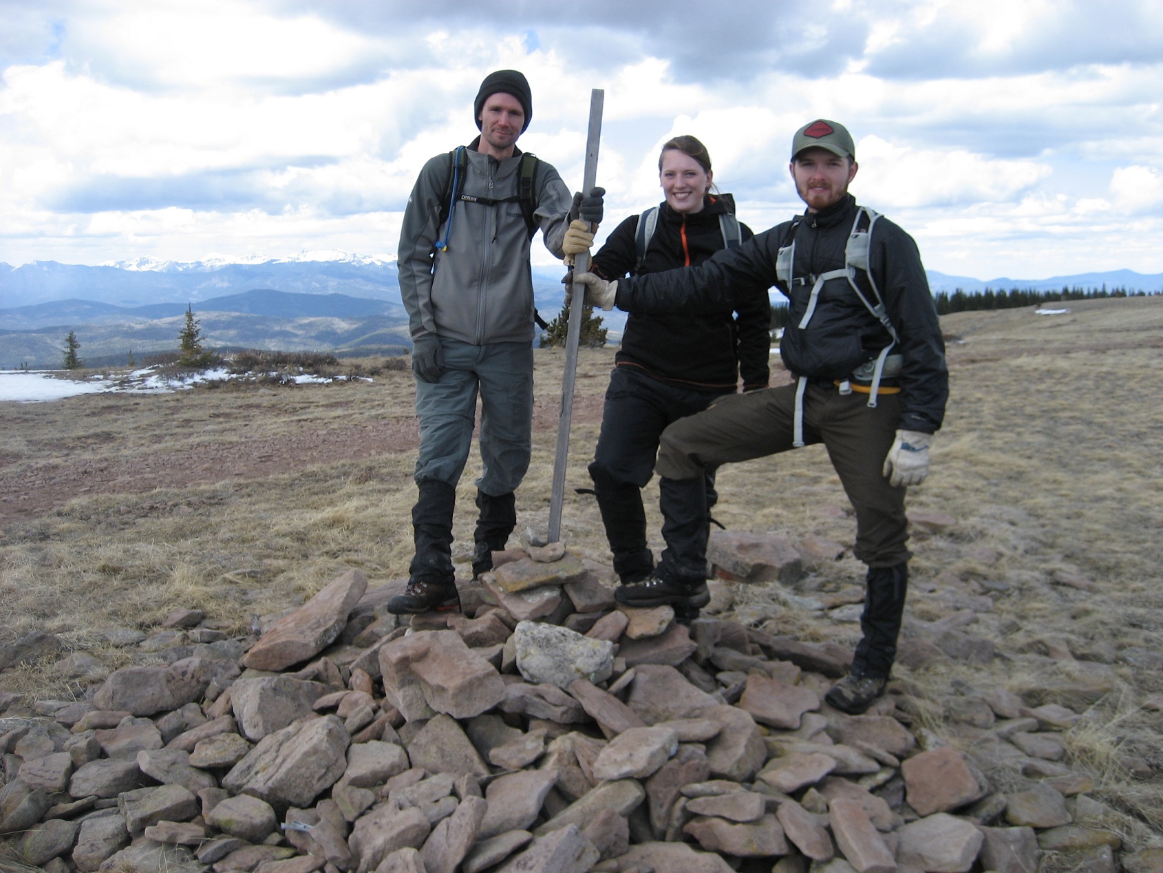 Three people standing on a pile of rocks in a valley.