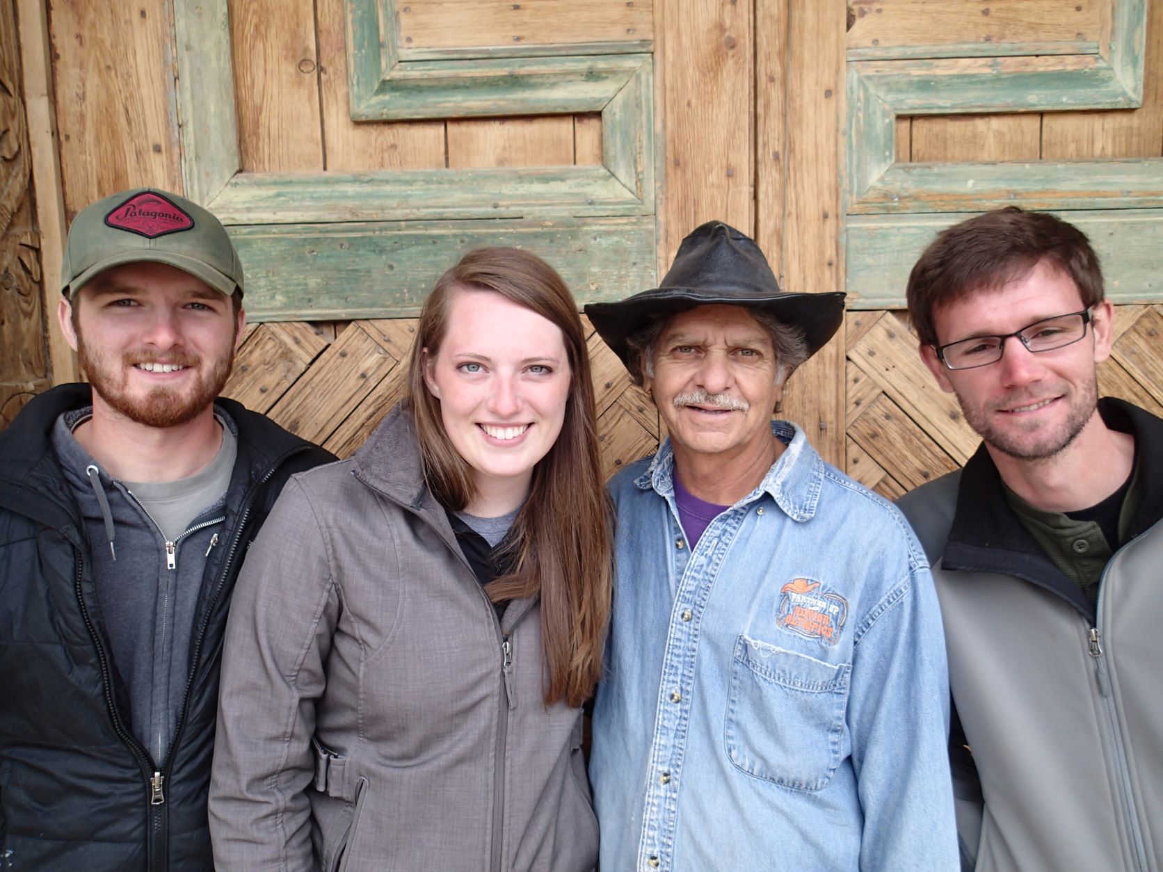 Four people standing, smiling at the camera, in front of the door.