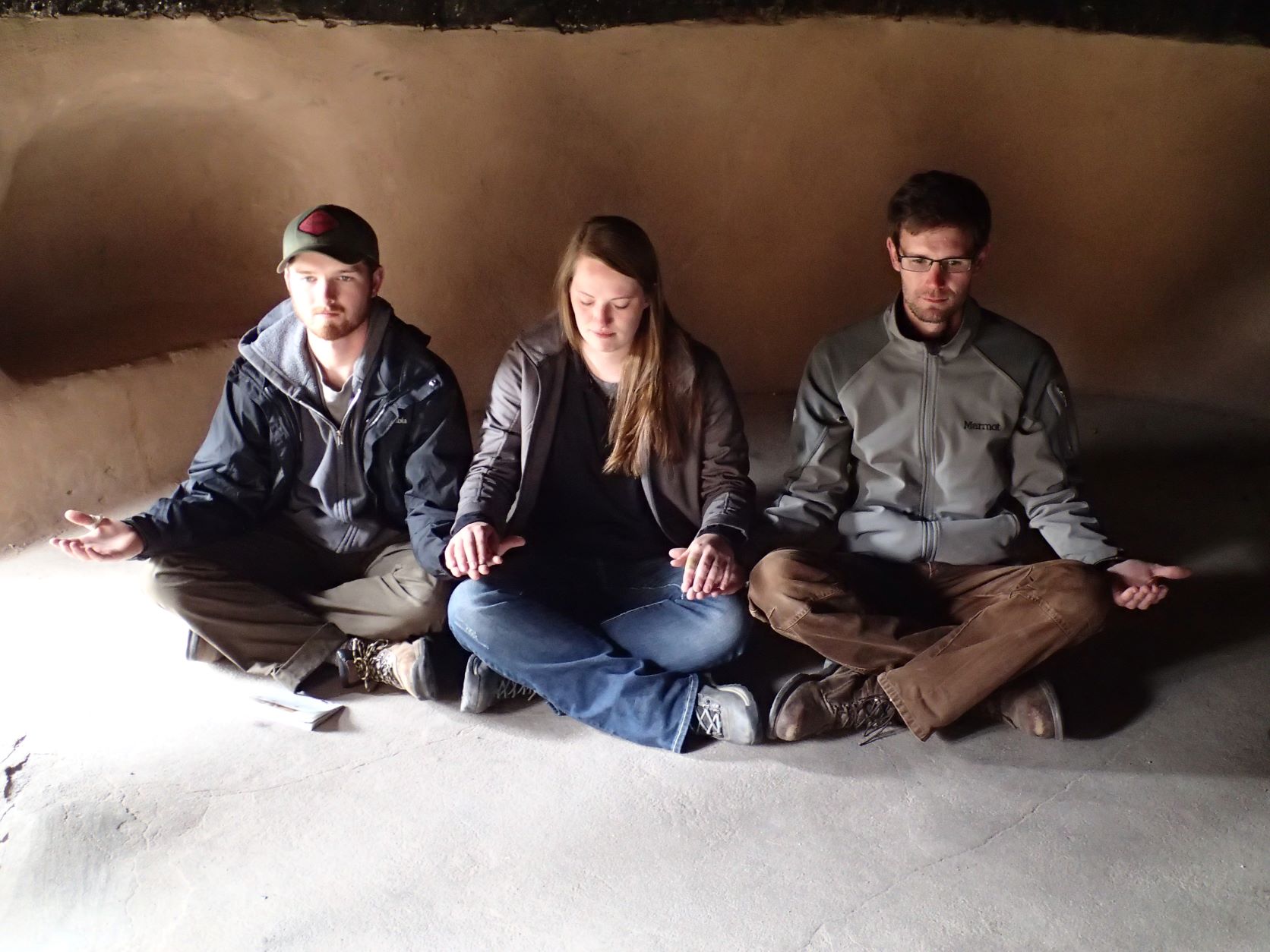 Three people sitting with their legs crossed in a cave.